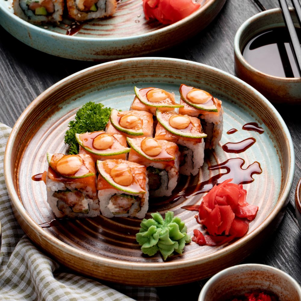 side view of sushi rolls with shrimps avocado and cream cheese served with ginger and wasabi on a plate on wooden background